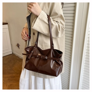 Detail of dark brown glossy leather underarm bag with decorative strap and slim handles