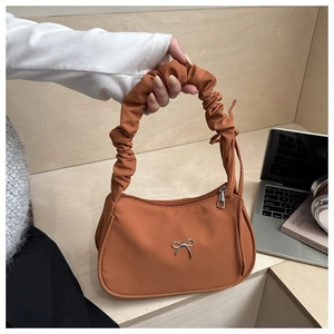 Detail of caramel orange dumpling bag featuring a ruffled handle and silver bow charm