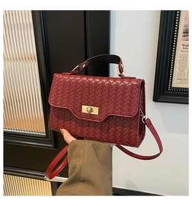 Détail d'un sac à main tressé bordeaux avec fermoir doré et bandoulière en cuir