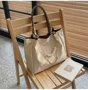 Detail of beige tote bag with pearl chain decoration and brown leather handles