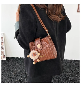 Detail der braunen gewebten Beuteltasche mit Fashion-Logo und Plüschlamm-Anhänger