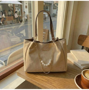 Close-up of beige suede tote bag with elegant pearl chain and metallic logo on table