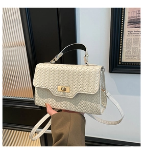 Détail d'un sac à main tissé beige avec fermoir rotatif doré et boucle métallique raffinée