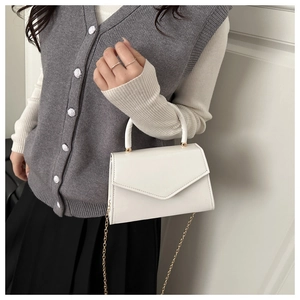 Close-up of a white leather envelope bag with a gold chain strap and a sleek top handle