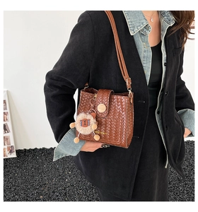 Detail of brown woven bucket bag with adjustable strap and cute lion plush charm