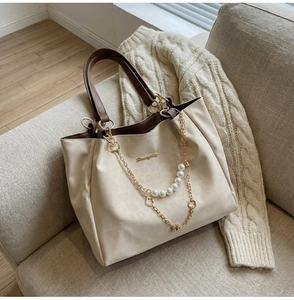 Close-up of cream tote bag with pearl chain, flower charm, and gold logo detail