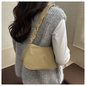 Close-up of khaki underarm bag with silver bow detail worn over a grey sweater vest
