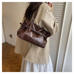 Dettaglio di una borsa a secchiello in pelle verniciata marrone con fibbia metallica