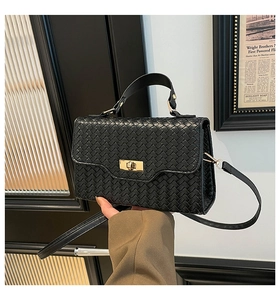 Détail d'un sac à main tressé noir avec un fermoir doré et une poignée élégante