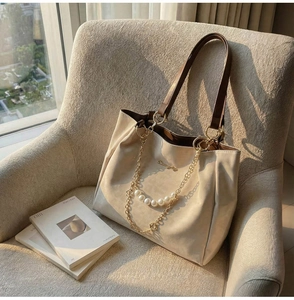 Detailed view of cream tote bag with pearl chain decoration on a beige textile armchair