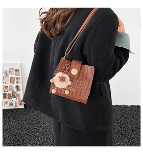 Brown woven bucket bag with cute plush pendant shown on shoulder of model in black jacket