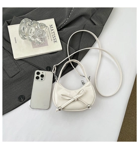 Détail du sac demi-lune blanc avec nœud en cuir et pendentifs métalliques argentés