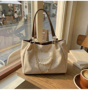Detail of beige suede tote bag with decorative gold chains and pearl accents in a cafe