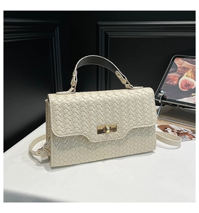 Gros plan du sac à main tissé crème avec fermoir rotatif doré et texture chic