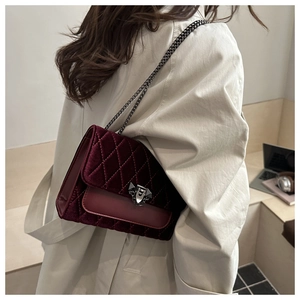 Detail of burgundy velvet quilted shoulder bag with chain strap and triangular metal clasp