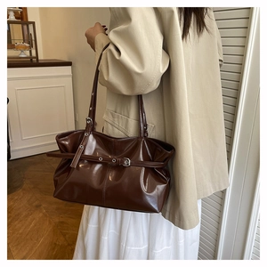 Detail of dark brown patent leather shoulder bag with buckle strap and glossy finish