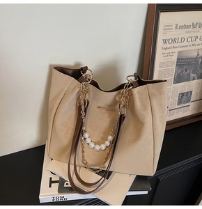 Detail of beige tote bag with matte finish, pearl chain, and gold logo on books