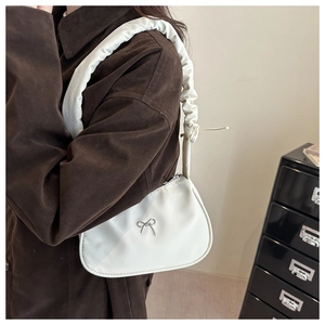 Close-up of white shoulder bag featuring a metallic butterfly and ruffled scrunchie strap