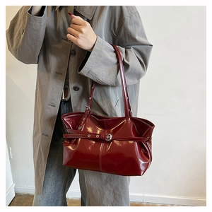 Detail of dark red patent leather tote bag with glossy finish and buckle element