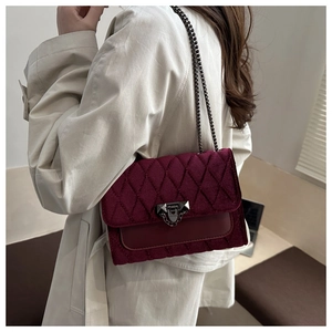 Detail of burgundy velvet crossbody bag with quilted diamond pattern on model