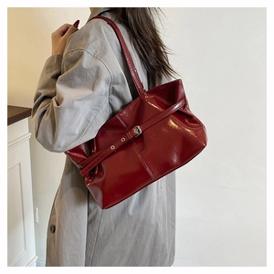 Dettaglio borsa tote in pelle verniciata rosso scuro abbinata a un trench coat grigio