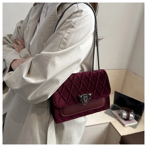 Detail of burgundy velvet quilted crossbody bag with metal chain strap and twist lock closure