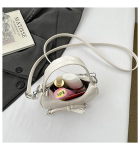 Vue détaillée du sac nœud en cuir verni crème montrant le rangement intérieur et la sangle