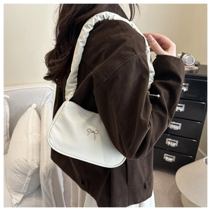 Detail of cream-white hobo bag featuring silver bow accent and padded scrunchie strap