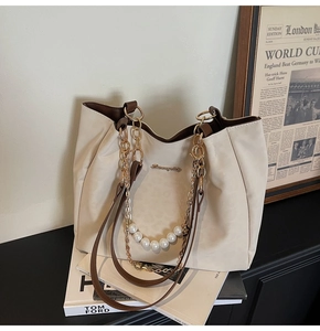 Detail of cream tote bag with pearl gold chain and leather handles on wooden desk