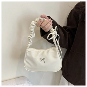 Close-up of cream nylon handbag featuring ruffled handles and silver bow metal ornament