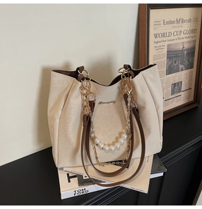Detail of off-white tote bag featuring pearl chain strap and brown leather handles