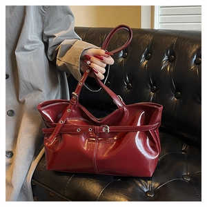 Close-up of wine red glossy leather tote bag featuring decorative buckles and retro texture