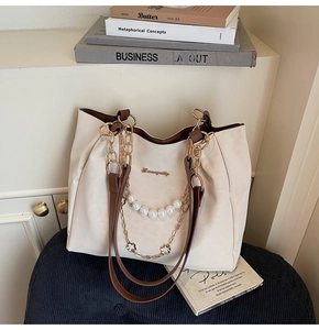 Detail of cream tote bag with elegant pearl chains and metallic flower charms