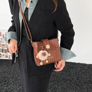 Détail d'un sac bandoulière marron tissé avec boucle en métal et breloque agneau