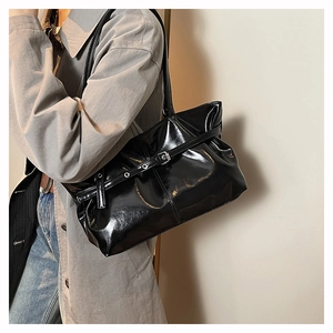 Close-up of black glossy oil wax leather tote bag with buckle straps and metal studs