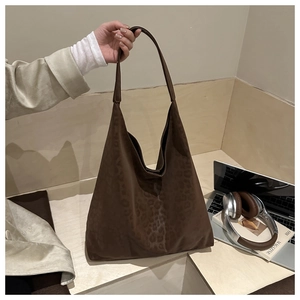 Close-up of a large leopard print tote bag in dark brown suede being held by a model
