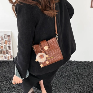 Détail d'un sac seau marron tissé avec pendentif en peluche porté par un mannequin