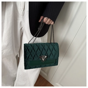 Close-up of dark green velvet handbag with quilted diamond stitching and metal chain strap