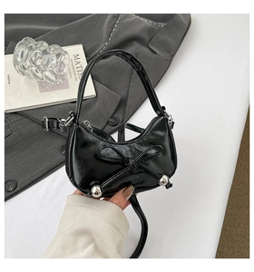 Gros plan d'un sac demi-lune noir brillant avec un grand nœud et des sphères argentées