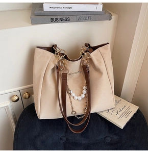 Detail of beige tote bag featuring pearl chain ornament and gold hardware logo