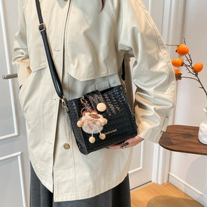 Sac seau noir tissé avec charm ours et bandoulière sur un trench-coat beige élégant