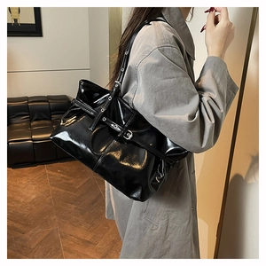 Modella che indossa una borsa a spalla in pelle verniciata nera con fibbia e occhielli