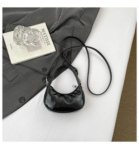 Détail d'un sac demi-lune noir plissé avec zip argenté sur fond de blazer gris