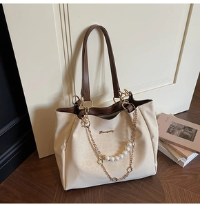 Close-up of beige canvas tote bag with pearl chain detail against a white door