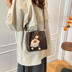 Détail du sac seau en cuir tressé marron foncé avec un joli pendentif en peluche