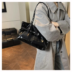 Detail of black patent leather shoulder bag with metal eyelets and rock-style buckle strap