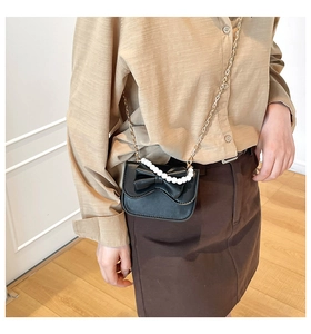 Detail of black leather crossbody bag with oversized bow and pearl handle chain
