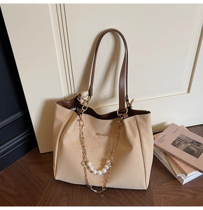 Detail of beige tote bag featuring pearl chain, brown handles, and metal logo