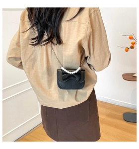 Detail of black crossbody bag with large bow and elegant pearl strap on a shoulder