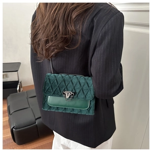 Close-up of quilted dark green velvet and leather flap bag with metal chain strap